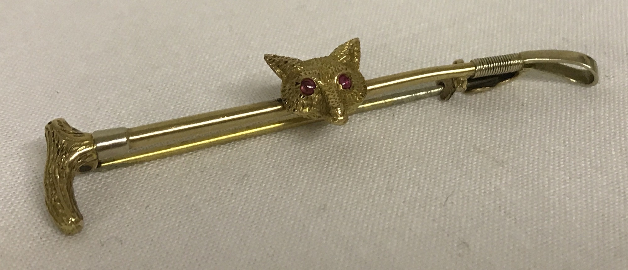 A 9ct gold riding crop and foxes head brooch. Foxes head set with 2 small rubies for eyes.