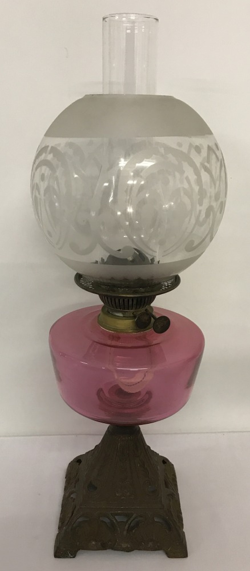 An Edwardian oil lamp with cast iron decorative base and cranberry coloured glass bowl.