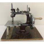 A vintage miniature/toy hand sewing machine mounted on a wooden plinth.