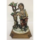 A Capodimonte Bellinaso figurine of a boy sat under a tree with a birds nest.