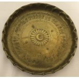 A brass circular dish with hammered Persian decoration to interior and shaped rim.
