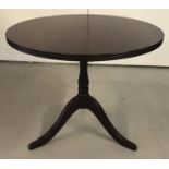 A modern mahogany coloured solid wood circular coffee table on tripod feet.