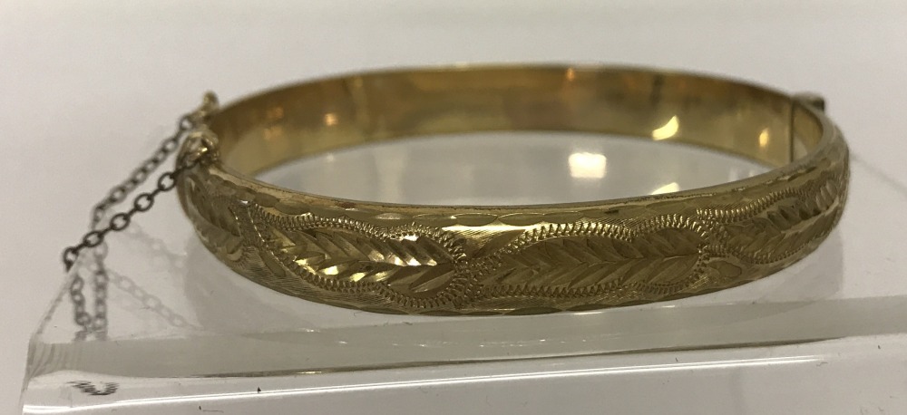 A vintage 9ct rolled gold, hinged bangle with half engraved decoration and safety chain.