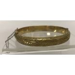 A vintage 9ct rolled gold, hinged bangle with half engraved decoration and safety chain.