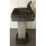 A square topped concrete bird bath.