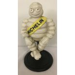 A cast iron sitting Michelin Man figurine on pedestal stand.