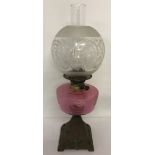 An Edwardian oil lamp with cast iron decorative base and cranberry coloured glass bowl.