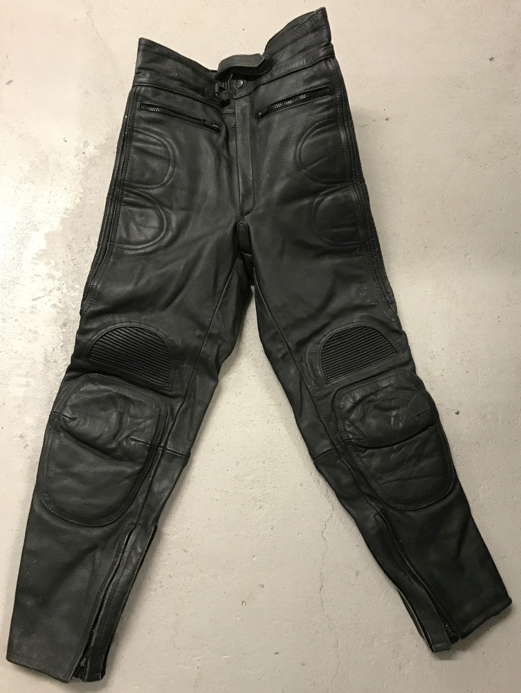 A pair of black leather motorcycle trousers with padded knees, ankle zips and zipped pockets.