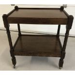 A vintage dark oak 2 tier tea trolley on wheels with carved detail to front.