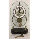 A Skeleton mantle clock. Brass workings with enamelled face and wooden plinth.