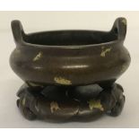 A small bronze 3 footed censer, with gold splatted detail, on a stand.
