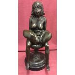 A bronze figurine of a nude woman sat on a stool, mounted on a circular marble plinth.