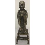 A Chinese white metal figure of a Buddha standing on a plinth.
