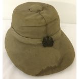 A vintage military khaki pith helmet with leather interior & strap and cap badge to front.
