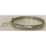 A vintage silver hinged bangle with engine turned decoration and safety chain.