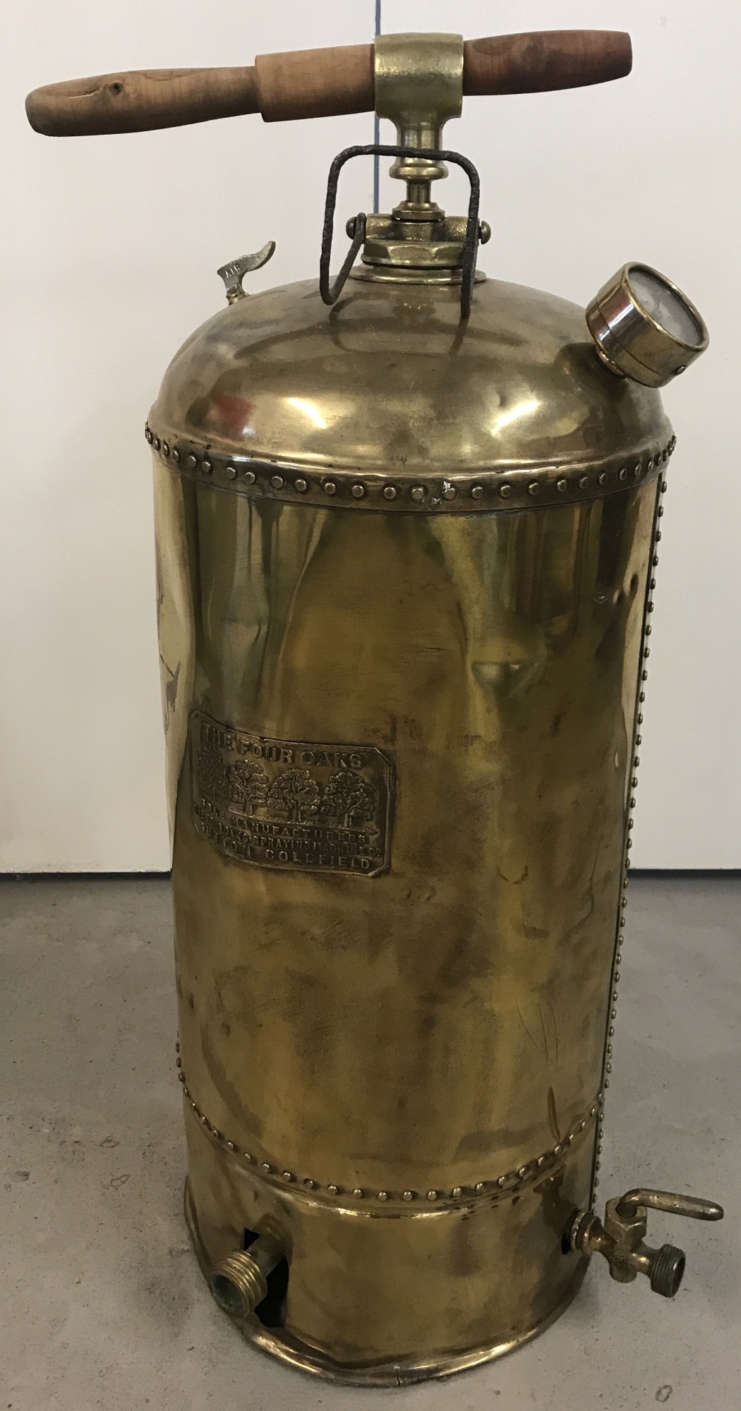 A large vintage brass sprayer labelled "The Four Oaks".