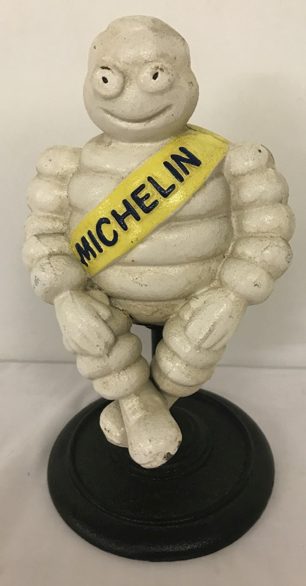 A cast iron sitting Michelin Man figurine on pedestal stand.