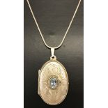 A silver oval locket with central oval cut blue topaz and front and back engraving.