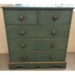 A pine chest of drawers with bun handles in a green lime wash finish.