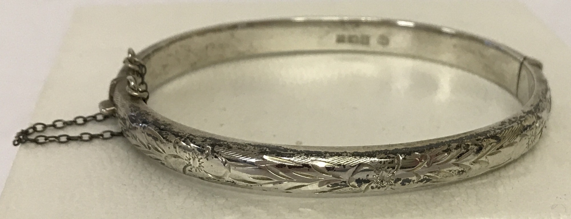 A vintage silver half engraved bangle complete with safety chain.