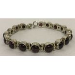 A modern tennis style silver bracelet set with 17 garnet cabochon stones. With lobster clasp.