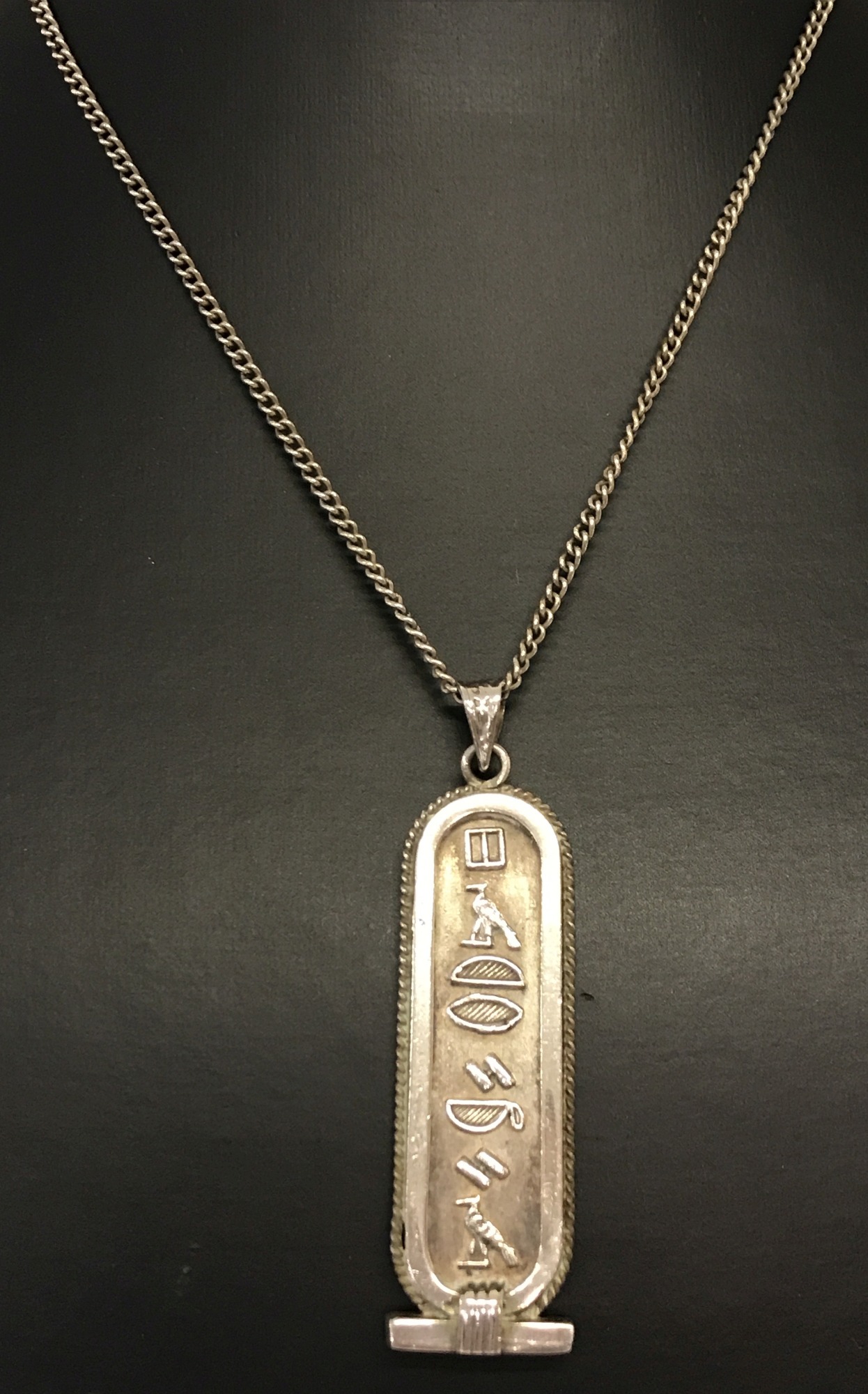 An Egyptian silver pendant with hieroglyph decoration to both sides. On a 20 inch curb chain.