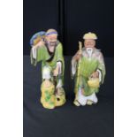 Two Oriental figures, one standing with a vase the other with his leg high up on a rock, 36cm
