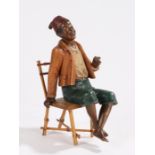 Bloc pottery figure, depicting a gentleman wearing a red fez, seated in a bamboo chair, the figure