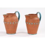 Pair of terracotta jugs with turquoise coloured glaze decoration, mask form spouts and loop handles,