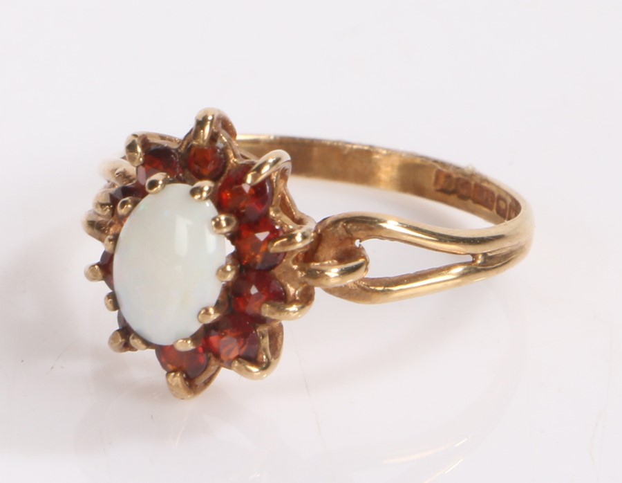 9 carat gold ring with tear drop pierced shoulders under an opal set in garnet surround. ring size L