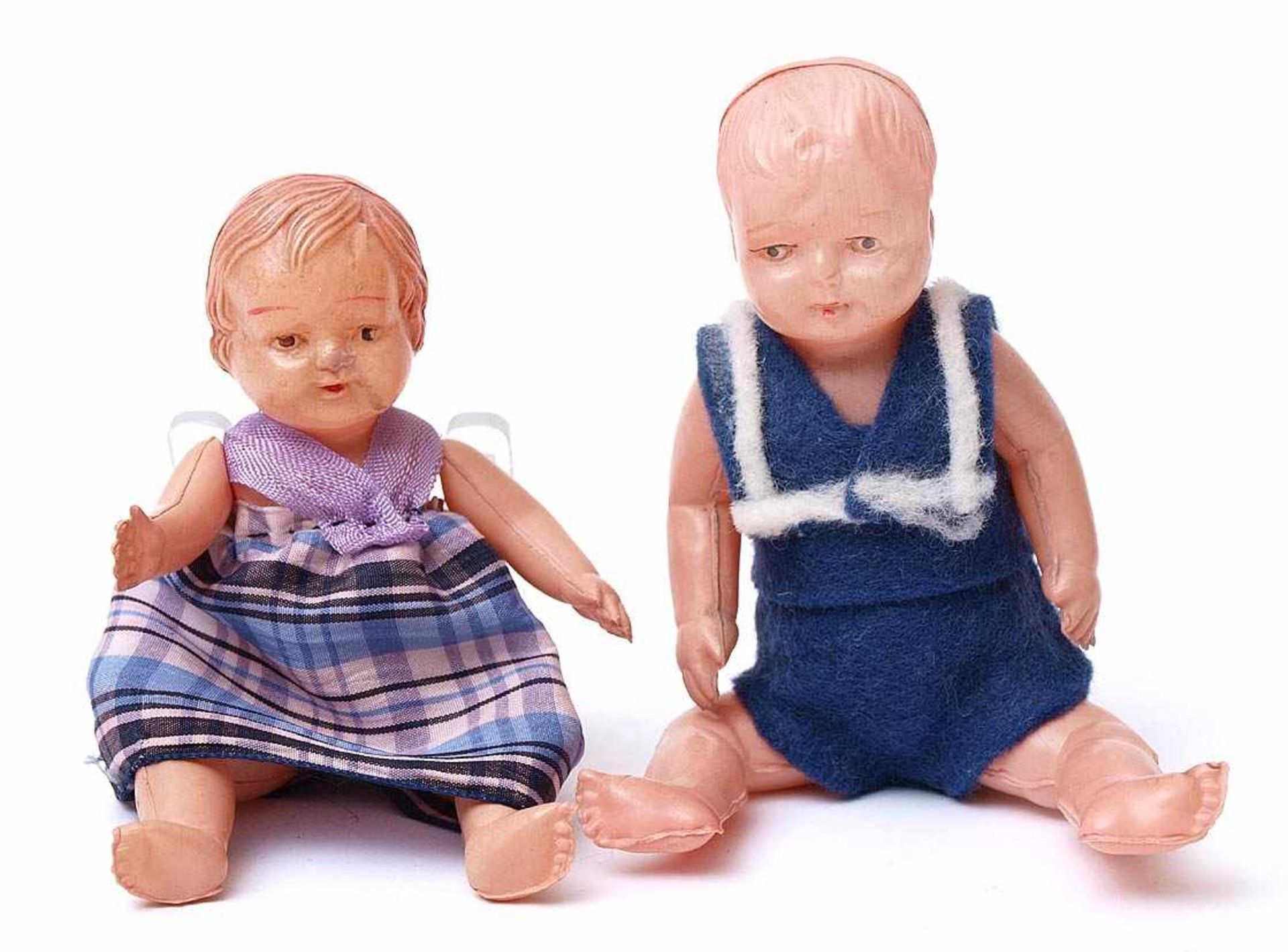 Zwei BabypüppchenGliederkörper aus Zelluoid. H.11 bzw. 12cm. Bekleidet.