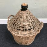 A Vintage green glass wine demi john bottle within a two section weaved basket. Measures 41cm in