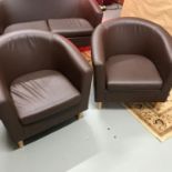 A Lot of two faux brown leather tub chairs.