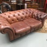 A Chesterfield button back tan leather two seater settee. On brass castor feet.