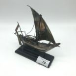 A Silver made model junk boat sat upon a hardwood stand. Measures 15cm in height