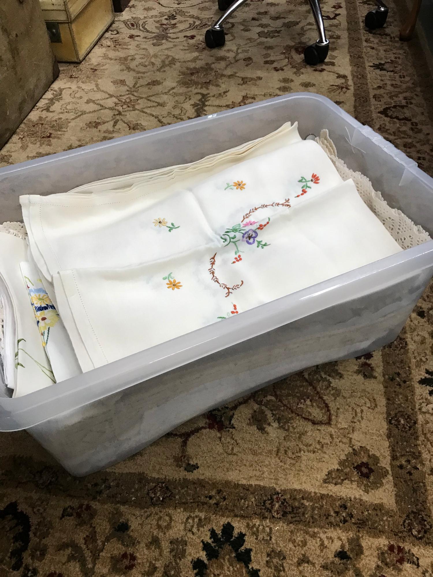 A Plastic tub filled with a selection of vintage hand stitched table clothes and throws