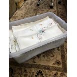 A Plastic tub filled with a selection of vintage hand stitched table clothes and throws