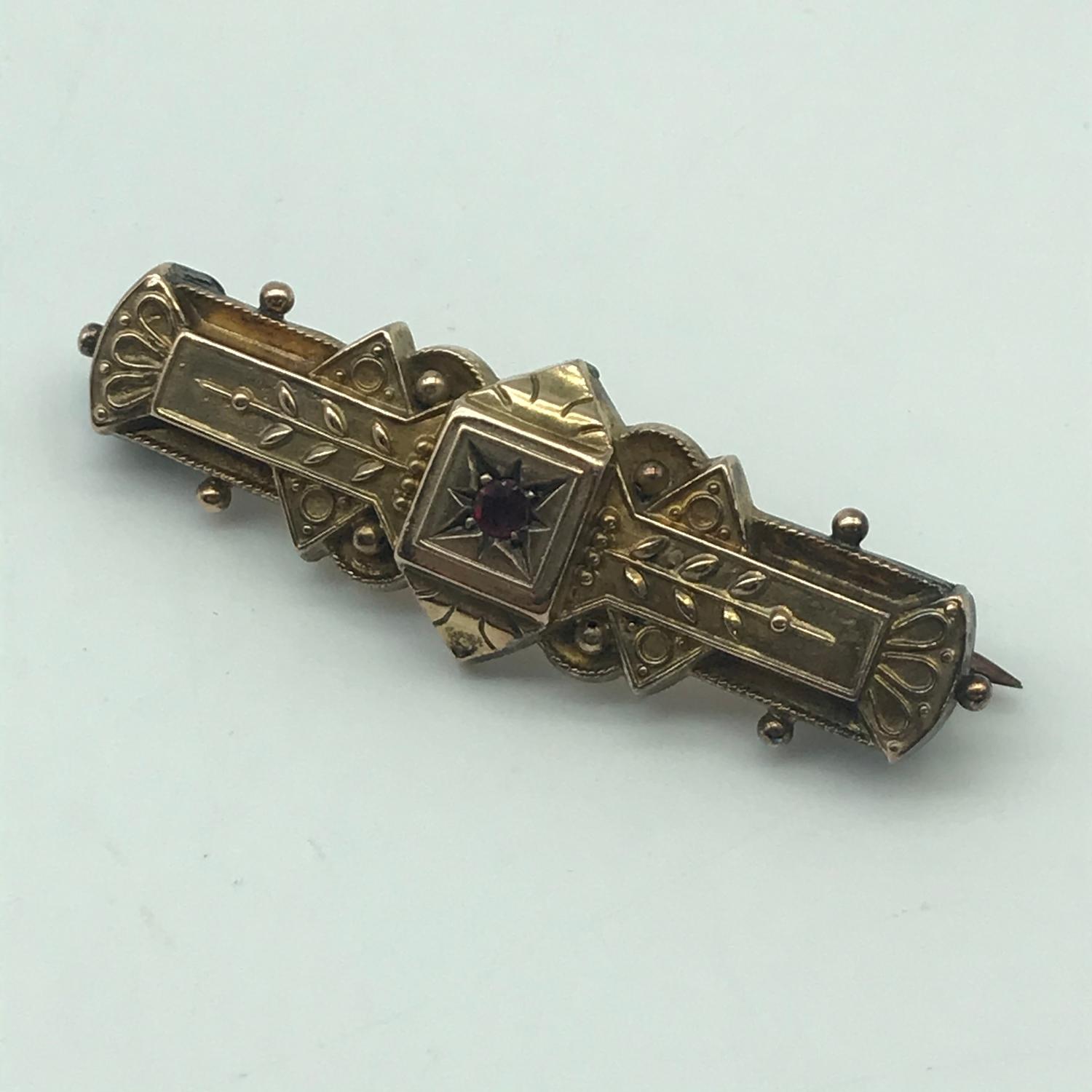 A Victorian 9ct gold ladies ornate bar brooch with single garnet stone setting. Weighs 3.41grams