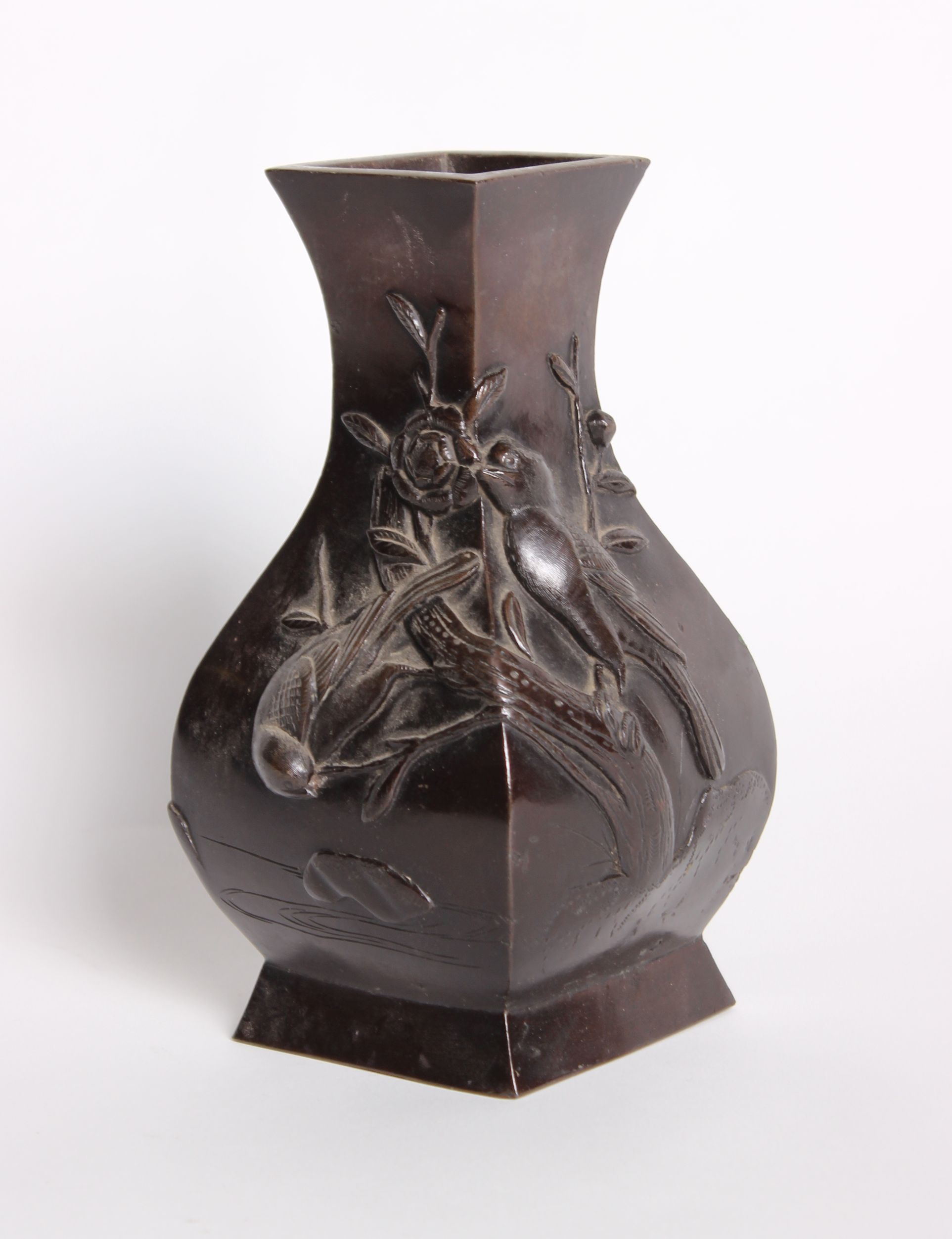 A Japanese bronze vase of baluster angled form, decorated in relief with birds, flowers and foliage,