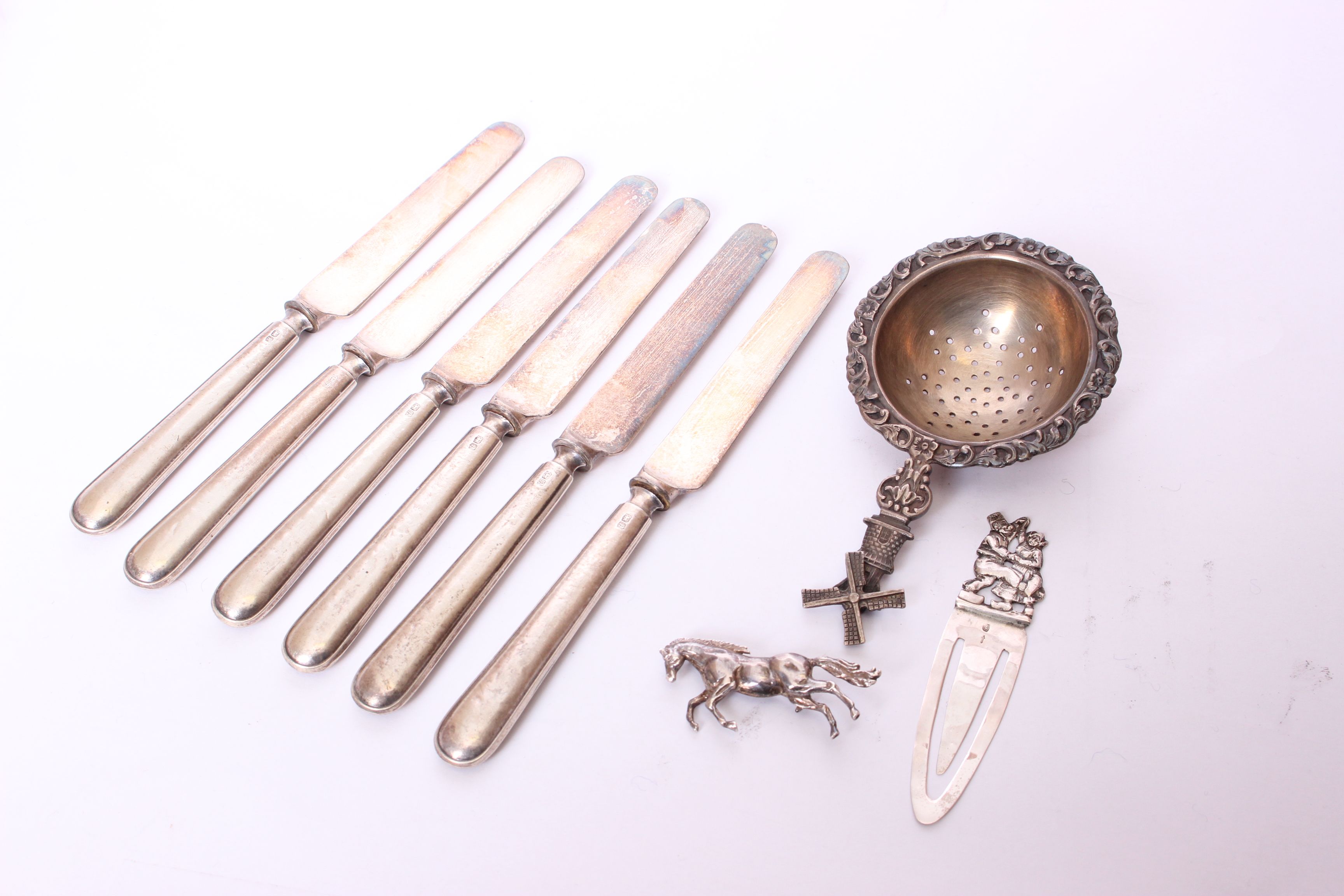 A set of six silver handled butter knives, an electroplated tea strainer, a bookmark and a white