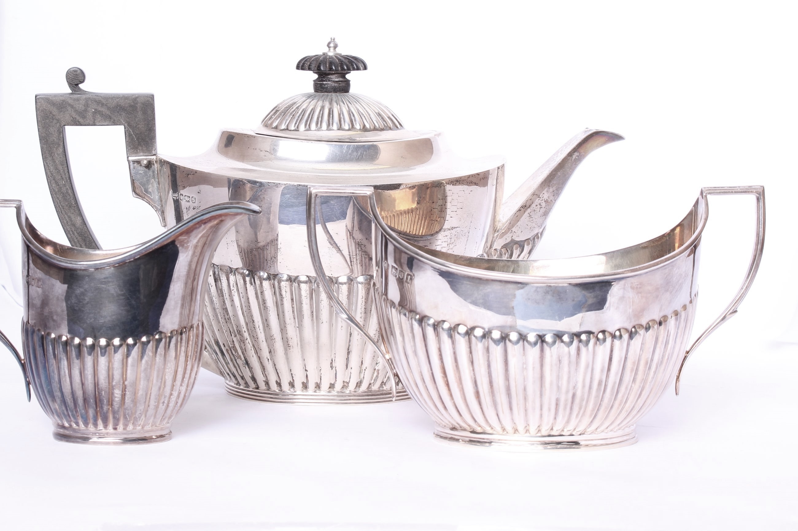 A three piece sterling silver tea set, with half reeded decoration and ebony handle, tea pot by