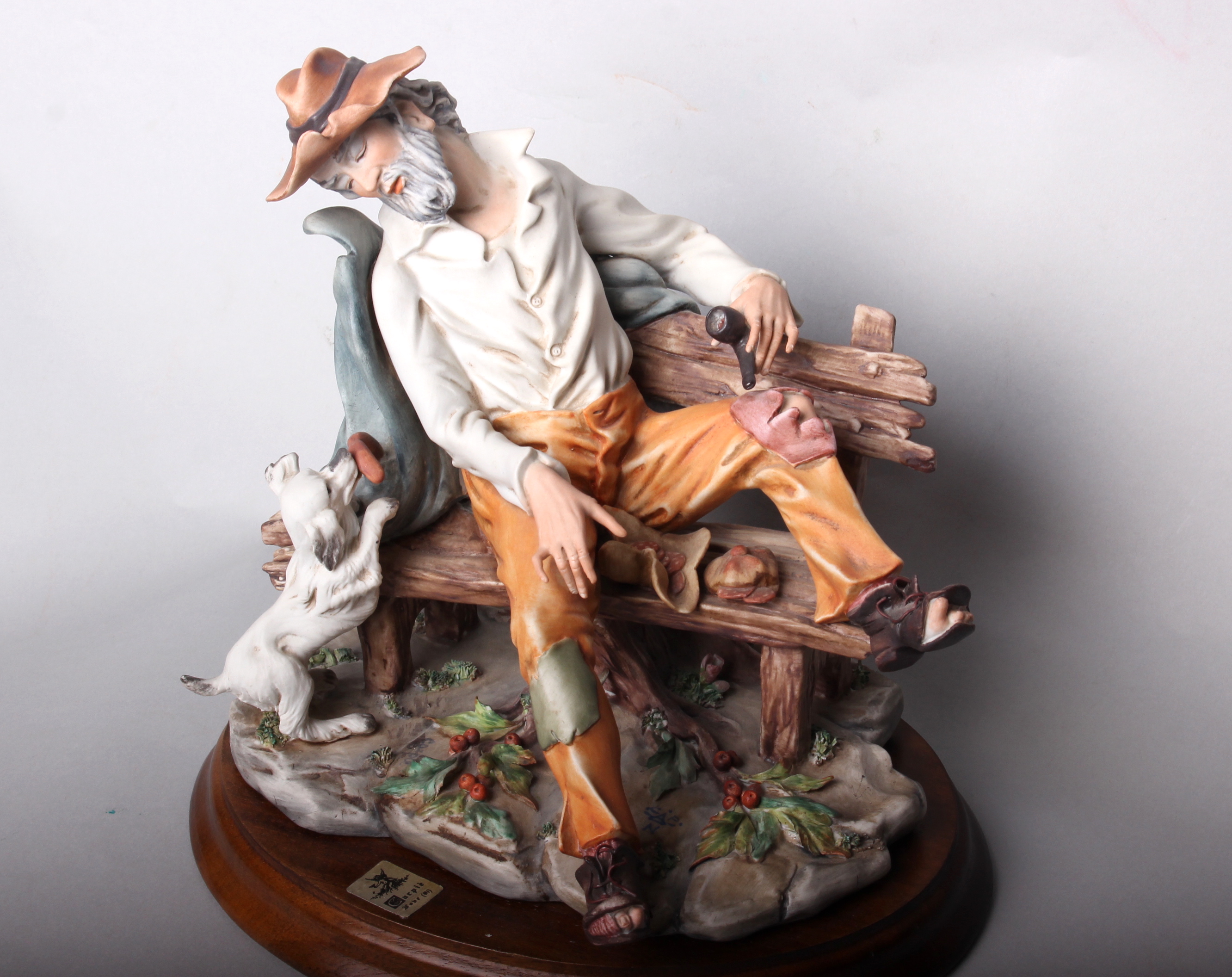 A Capodimonte style figure of a tramp on a bench with a dog, marked 'Italy 325/A', on turned