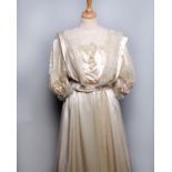 An early 20th Century ivory satin wedding outfit, the bodice trimmed with lace and organza bows