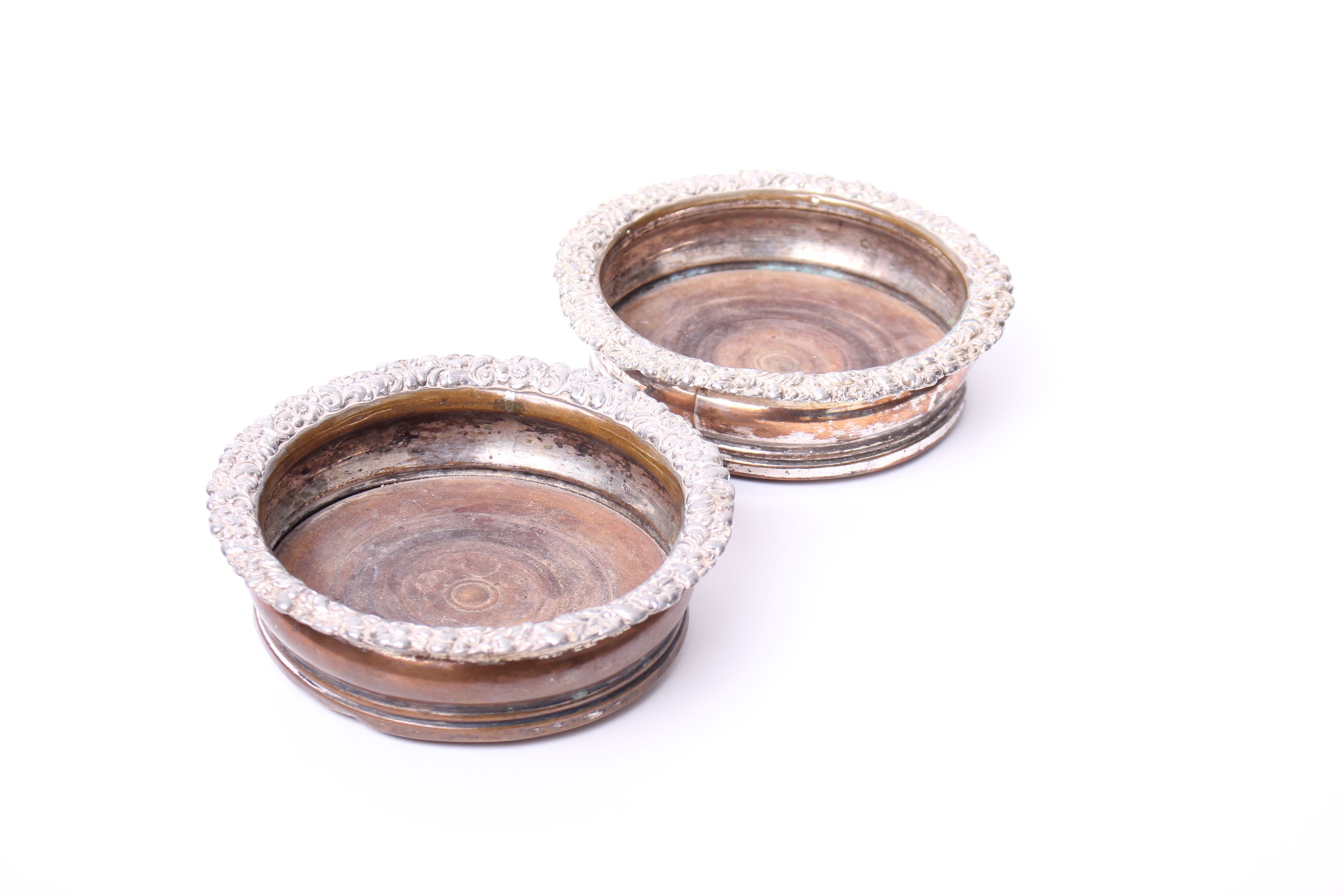 A pair of silver plated wine bottle coasters, with raised floral rim and turned wooden bases, a pair