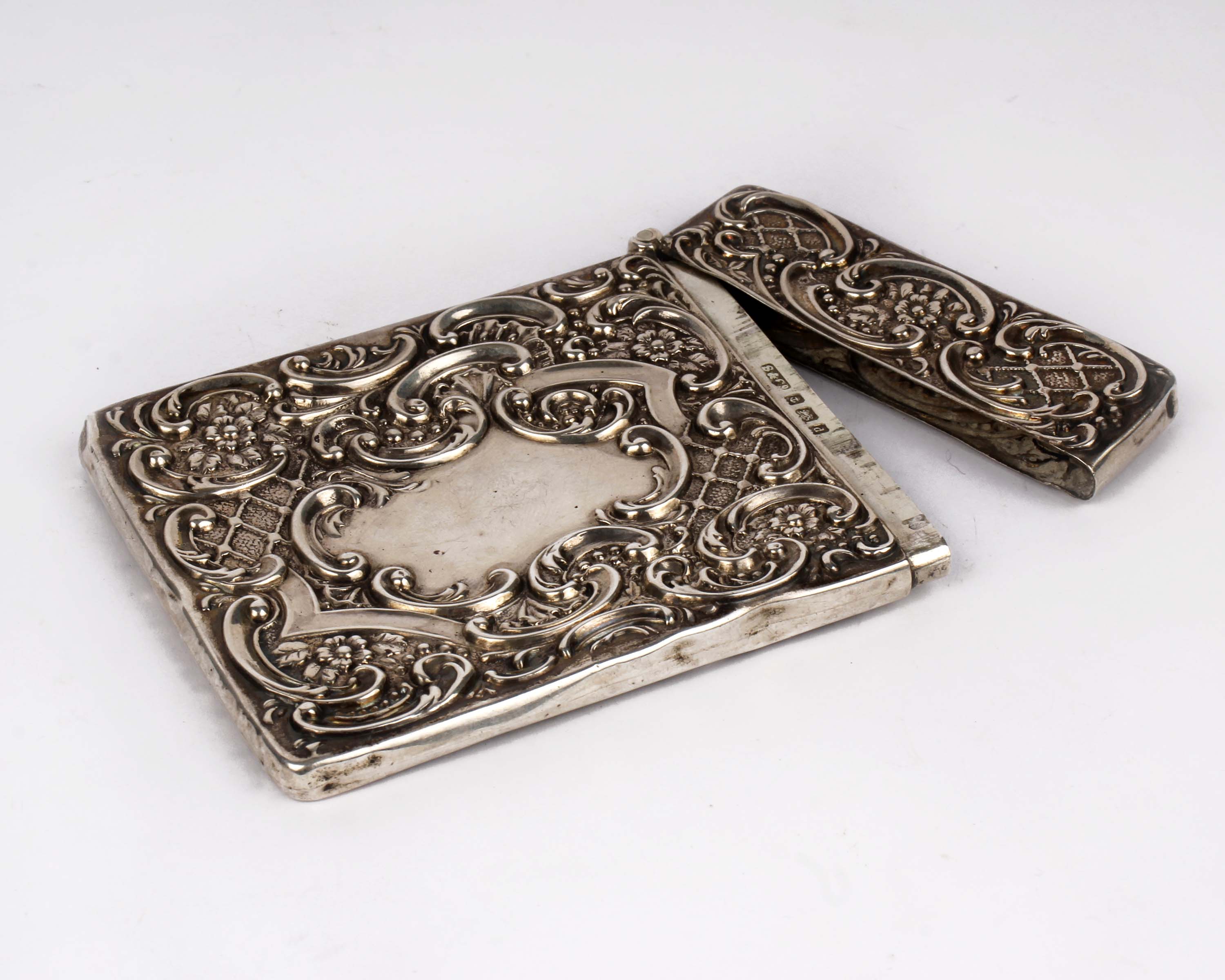 An Edwardian sterling silver card case with raised and engraved floral decoration and vacant central