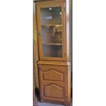 A Modern Oak Corner Cabinet, With a glazed top enclosing a shelved interior, above a panelled