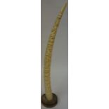 A Carved Ivory African Tusk, Decorated with African figures, raised on a wood base, 50cm high