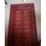 A Wilton Persian Style Rug, Decorated with nine rows of two geometric medallions, on a red ground,
