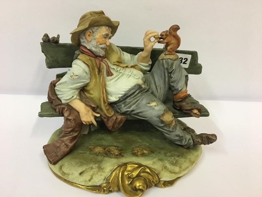 A Capo Di Monte Style Figure Group, Modelled as a drunk laying on a garden bench feeding a squirrel, - Image 2 of 4