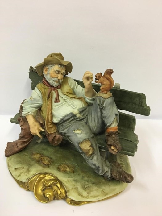 A Capo Di Monte Style Figure Group, Modelled as a drunk laying on a garden bench feeding a squirrel, - Image 3 of 4